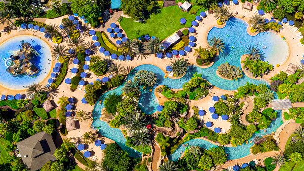 Ein Luftbild eines Resorts mit mehreren Schwimmbecken, Palmen und Liegestühlen.