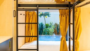 A bunk bed room with yellow curtains, a window with a view of greenery, and a door labeled 'C'. - Petit Hostel Palacio Real (Madrid)