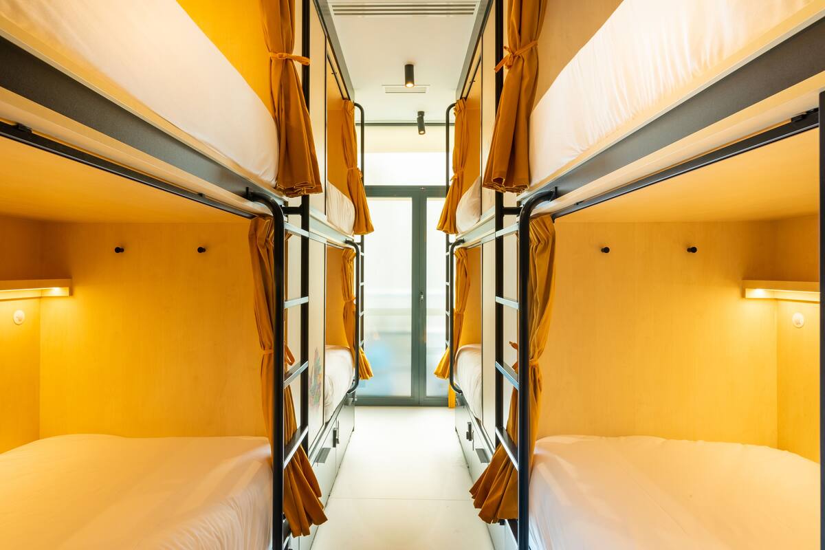 A train compartment with bunk beds, a central aisle, and overhead lighting.