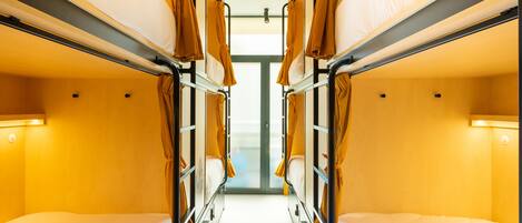 A train compartment with bunk beds, a central aisle, and overhead lighting.