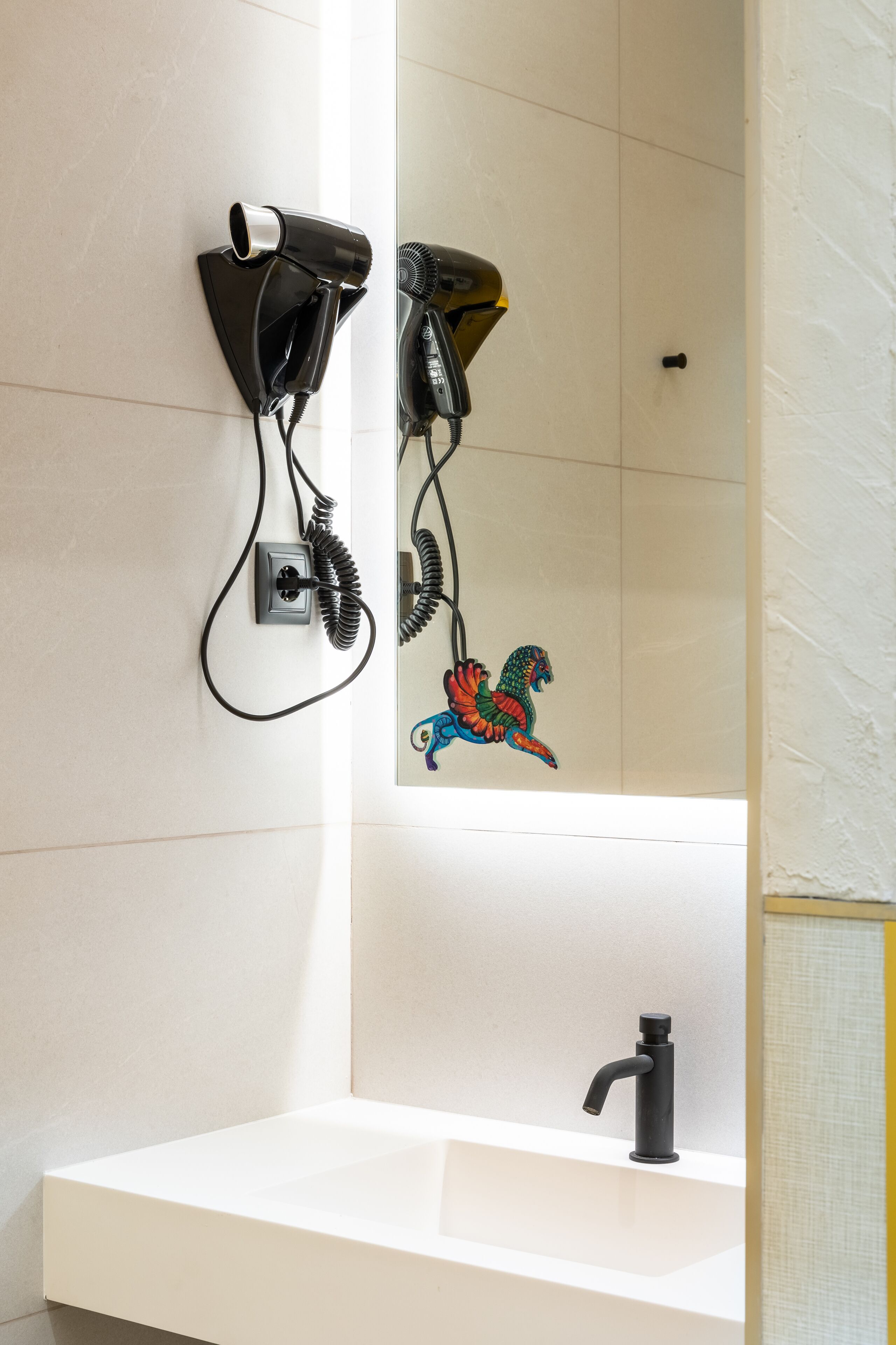 Un baño con un lavamanos blanco, un grifo negro y dos secadores de pelo fijados en la pared.