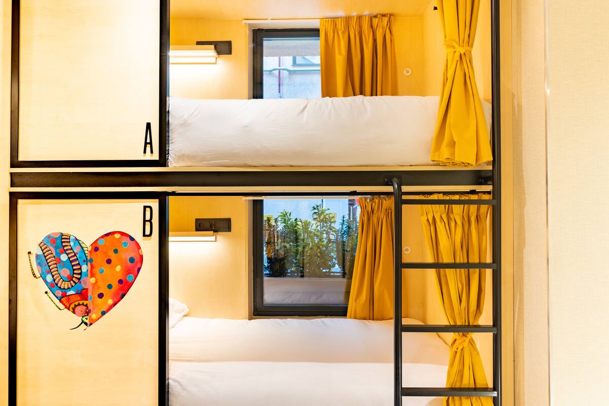 A dormitory-style room with two beds, a window with curtains, and a wall with a heart design.
