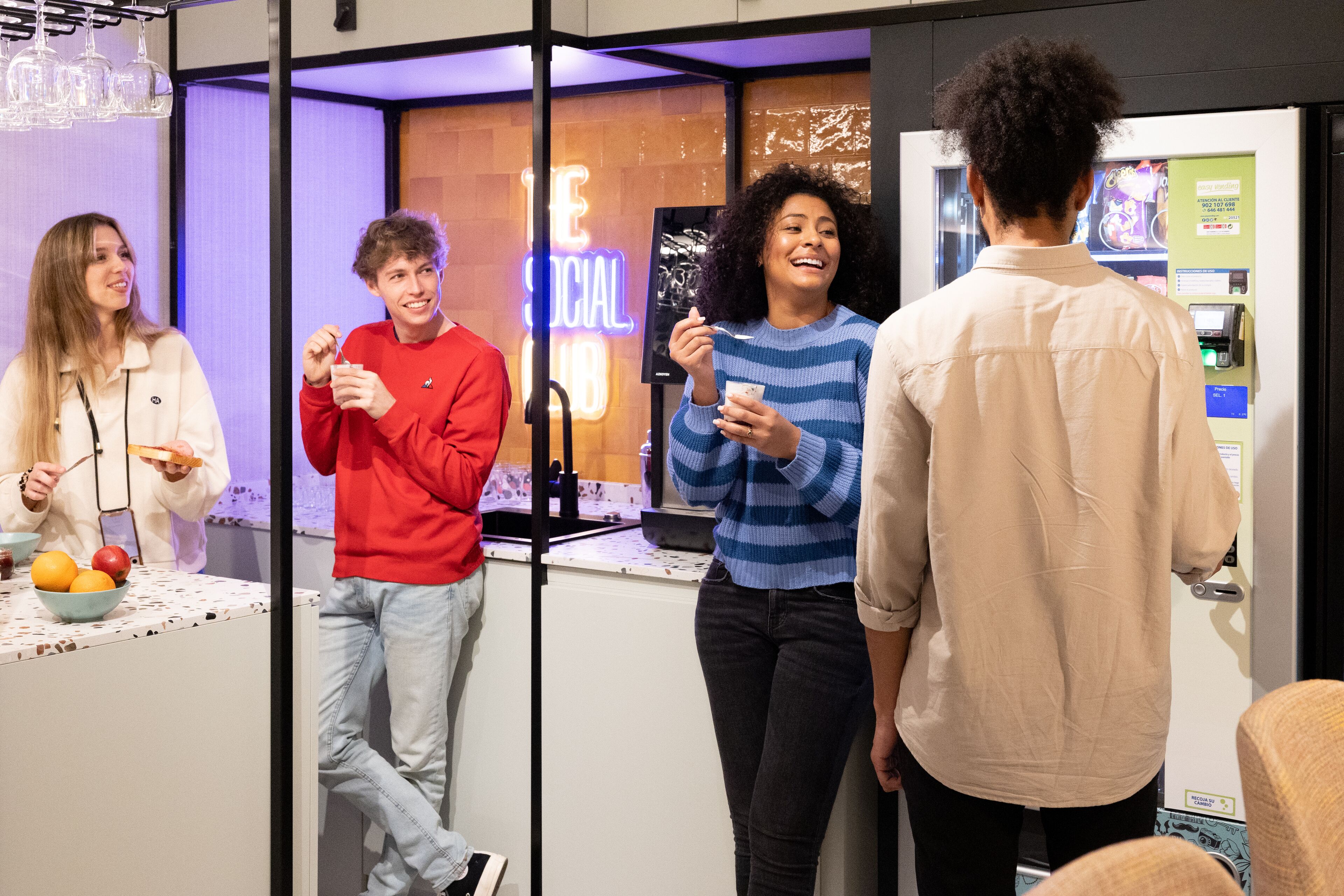 A group of people in a modern indoor setting with a counter and a neon sign.