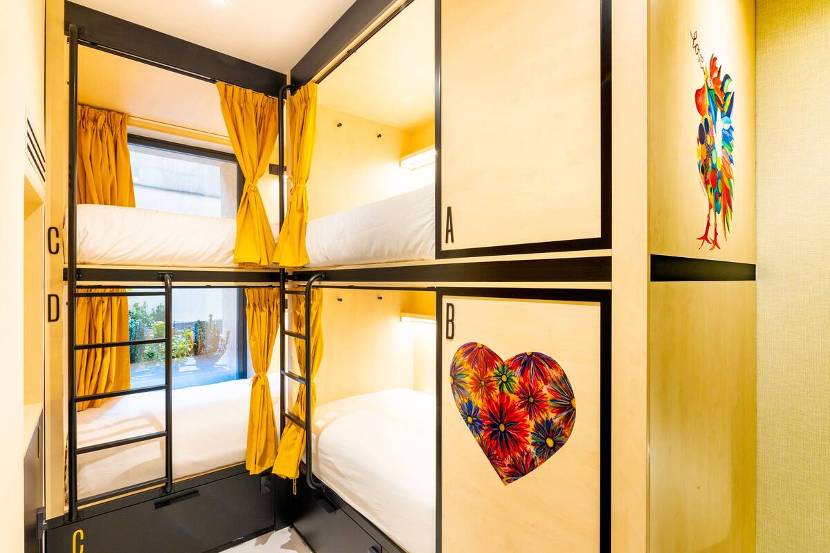 A bunk room with two beds, a window with curtains, and a wall with a colorful heart design.