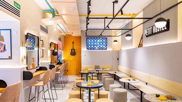 A modern cafe with multiple seating areas, including tables and stools, and a visible counter with a menu display. - Petit Hostel Palacio Real (Madrid)