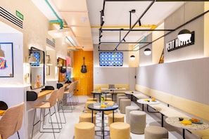 A modern cafe with multiple seating areas, including tables and stools, and a visible counter with a menu display.
