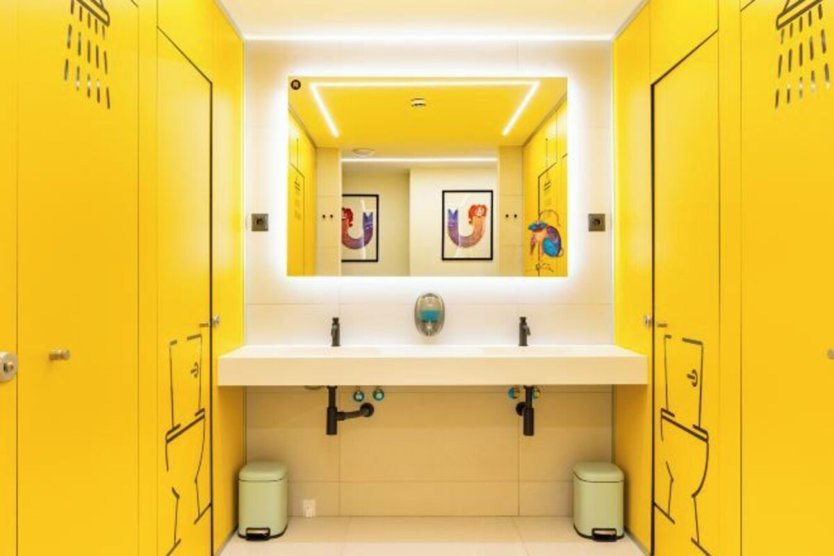 A bathroom with yellow lockers, a white sink, and two trash bins.