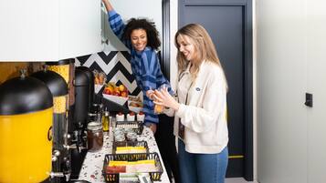 Una cocina con una cafetera, un frutero y diversos alimentos sobre la encimera.