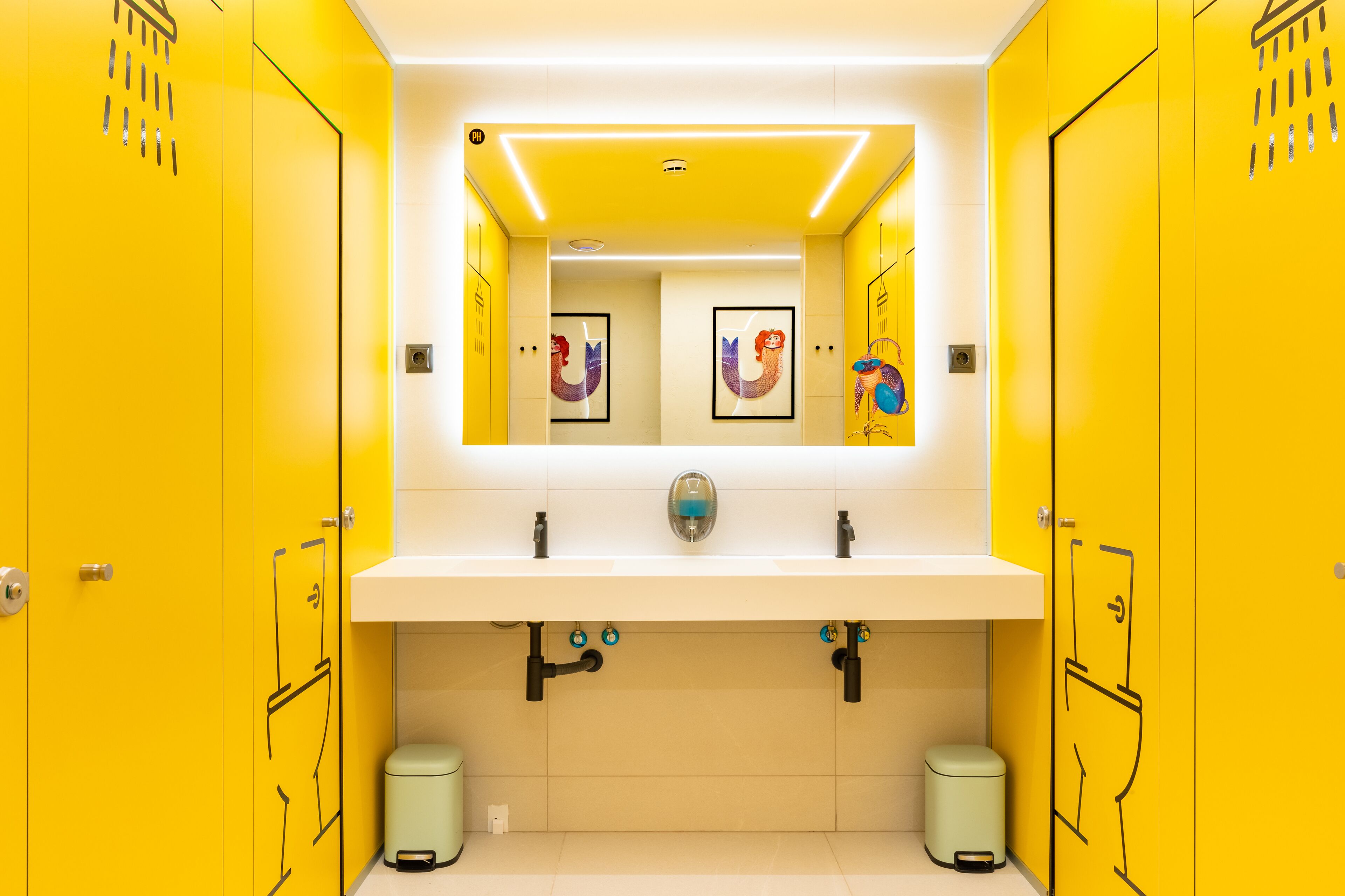 A brightly lit bathroom with yellow lockers, a white sink, and two trash bins.