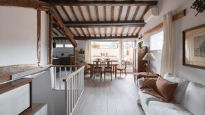 Un'ampia zona giorno con soffitto in legno, un divano bianco, un tavolo da pranzo con sedie e vista sull'esterno.
