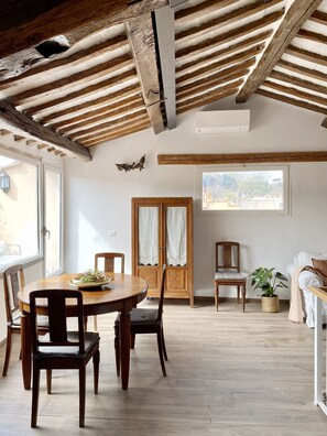 Ein Essbereich mit Holztisch und Stühlen, einer Holztür mit Vorhängen sowie ein Ausblick ins Freie durch ein Fenster.