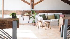 A spacious loft with exposed wooden beams, a white sofa, and a dining table with stools. - Penthouse in Trastevere with rooftop terrace🌱🌈 (Roma)