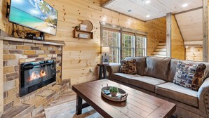 A cozy cabin interior with a stone fireplace, a large flat-screen TV, a wooden ceiling, and a comfortable seating area. - Ooh LA LA, Private Indoor Pool, Arcade Game, Foosball, Free Attraction Tickets!! (Sevierville)