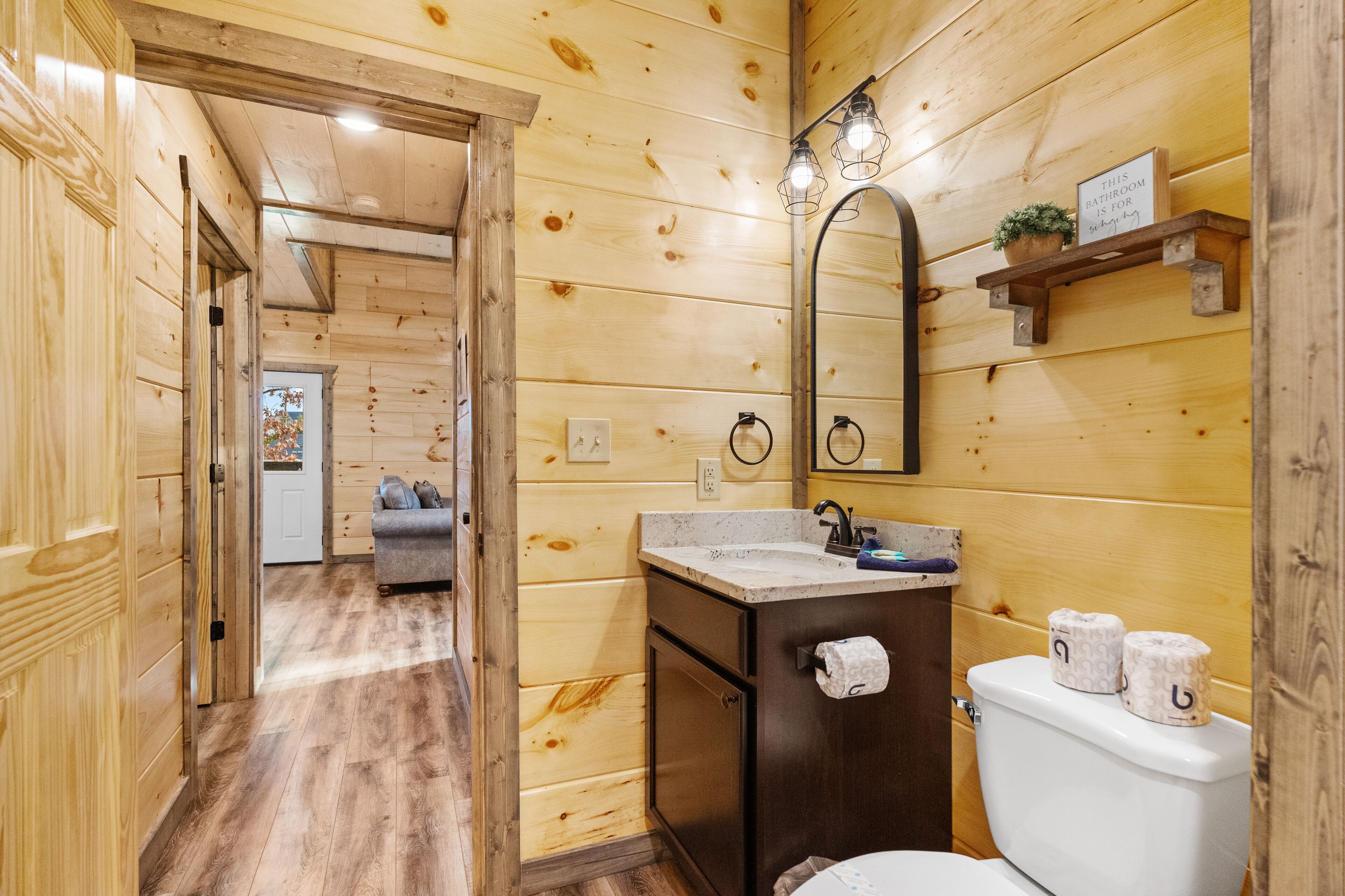A wooden-paneled bathroom with a sink, toilet, and mirror.