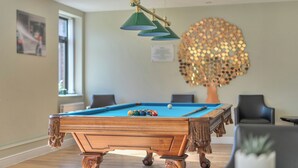 A pool table in a room with a decorative tree wall art, a hanging lamp, and a window. - Marine Court Two Bedroom Second-floor Apartment 33 (Littlehampton)