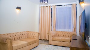 Un salón con dos sofás beige, un mueble de televisión de madera y un ventanal con cortinas.