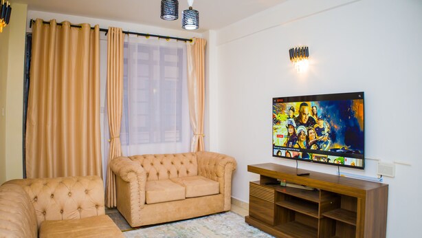 Una sala de estar con un sofá color beige, un mueble de entretenimiento de madera y un televisor de pantalla plana montado en la pared.