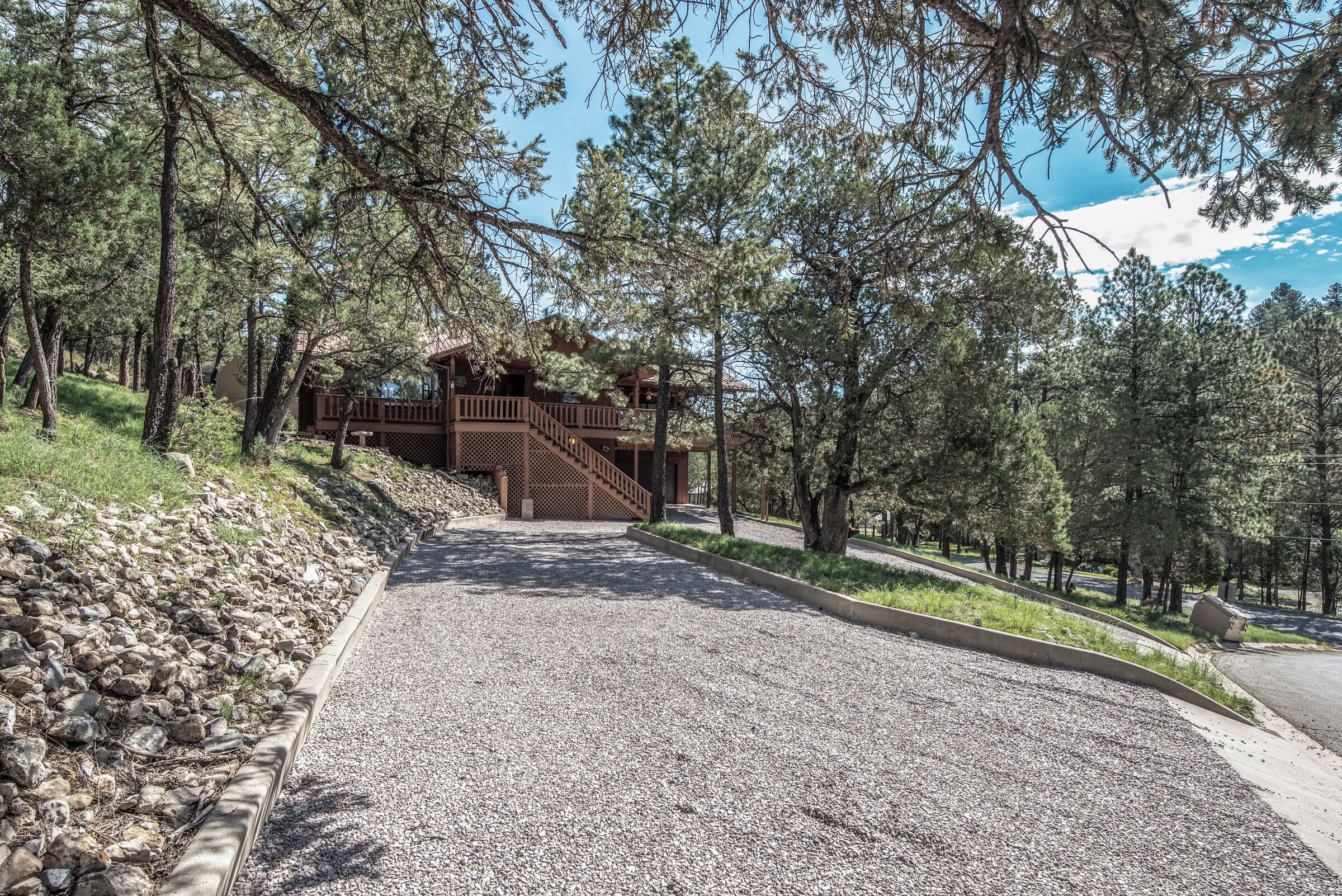 A gravel pathway leading to a wooden cabin with a balcony, surrounded by trees.