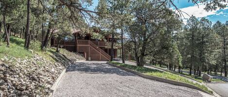 A gravel pathway leading to a wooden cabin with a balcony, surrounded by trees.