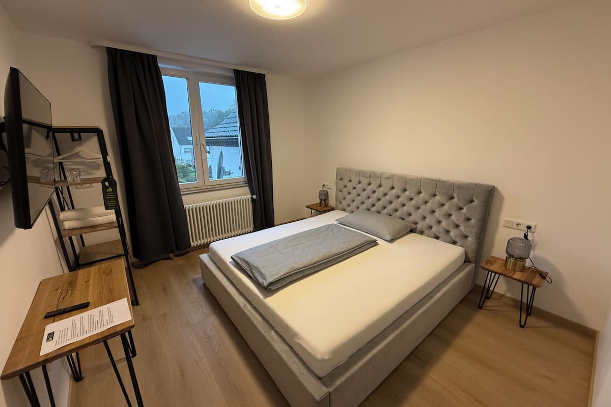Camera d'albergo moderna con un letto grande, una scrivania in legno, un tavolino e una finestra con tende.