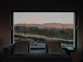 Un dormitorio con un ventanal que ofrece vistas a olivos y montañas.