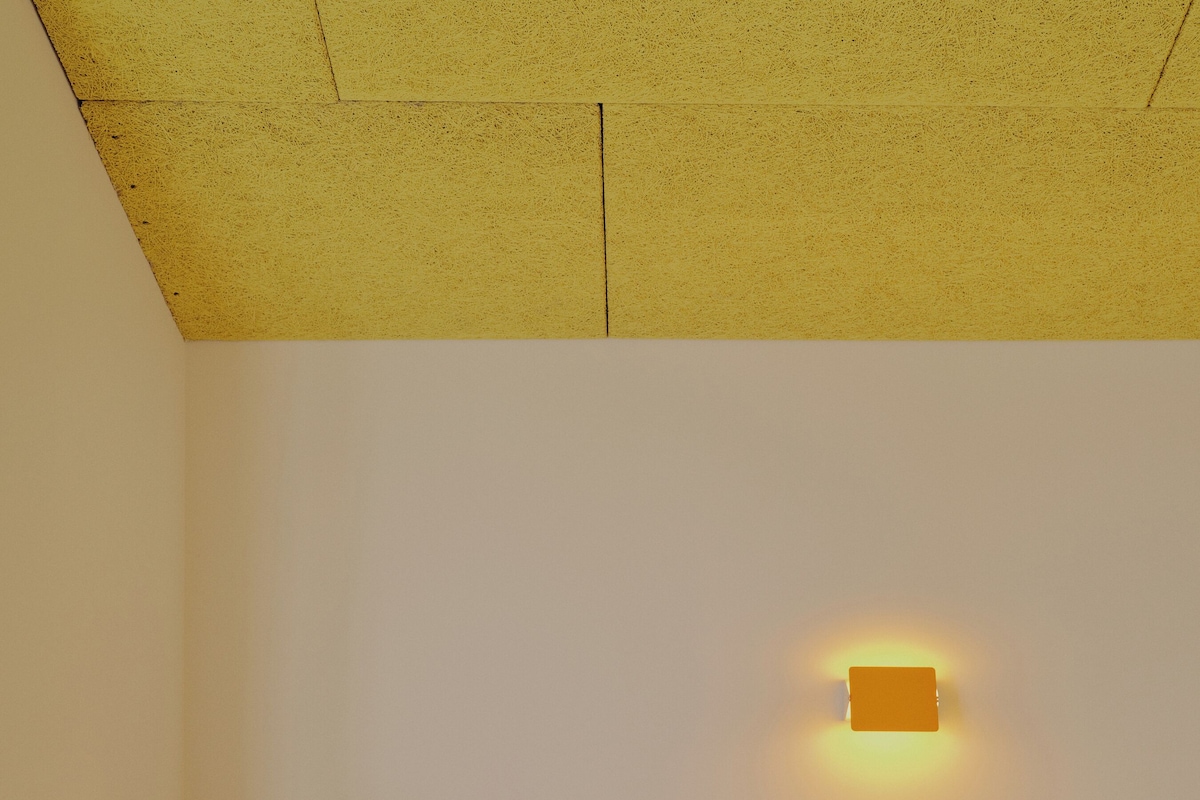 Un dormitorio con cama, mesita de noche, silla y una lámpara fijada a la pared.