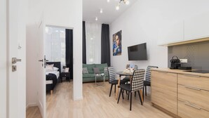 A modern living room with a sofa, a dining table with chairs, a TV mounted on the wall, and a kitchen area with cabinets and a countertop. - Comfortable Apartment in the Center | Close to Wawel Castle | Smart TV (Kraków)