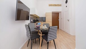 A compact kitchen with modern appliances, a dining area with houndstooth chairs, and a flat-screen TV mounted on the wall. - Comfortable Apartment in the Center | Close to Wawel Castle | Smart TV (Kraków)