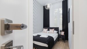 A modern bedroom with a black and white patterned wall, a bed with white and pink bedding, a small bedside table with a lamp, and a black curtain. - Comfortable Apartment in the Center | Close to Wawel Castle | Smart TV (Kraków)