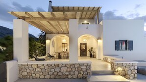 A modern outdoor patio with stone walls, a wooden pergola, and a dining area with chairs and a table. - Escape View Villa (Santorini)