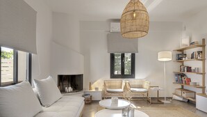 A modern living room with a sofa, two chairs, a fireplace, a bookshelf, and a hanging light fixture. - Escape View Villa (Santorini)
