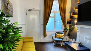Uma sala de estar moderna com um sofá amarelo, uma poltrona cinza com uma almofada amarela, uma escrivaninha preta e uma planta em vaso.