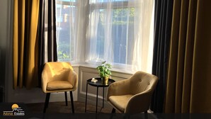 Quarto com duas poltronas, uma mesinha de centro com uma planta e uma janela com cortinas leves.