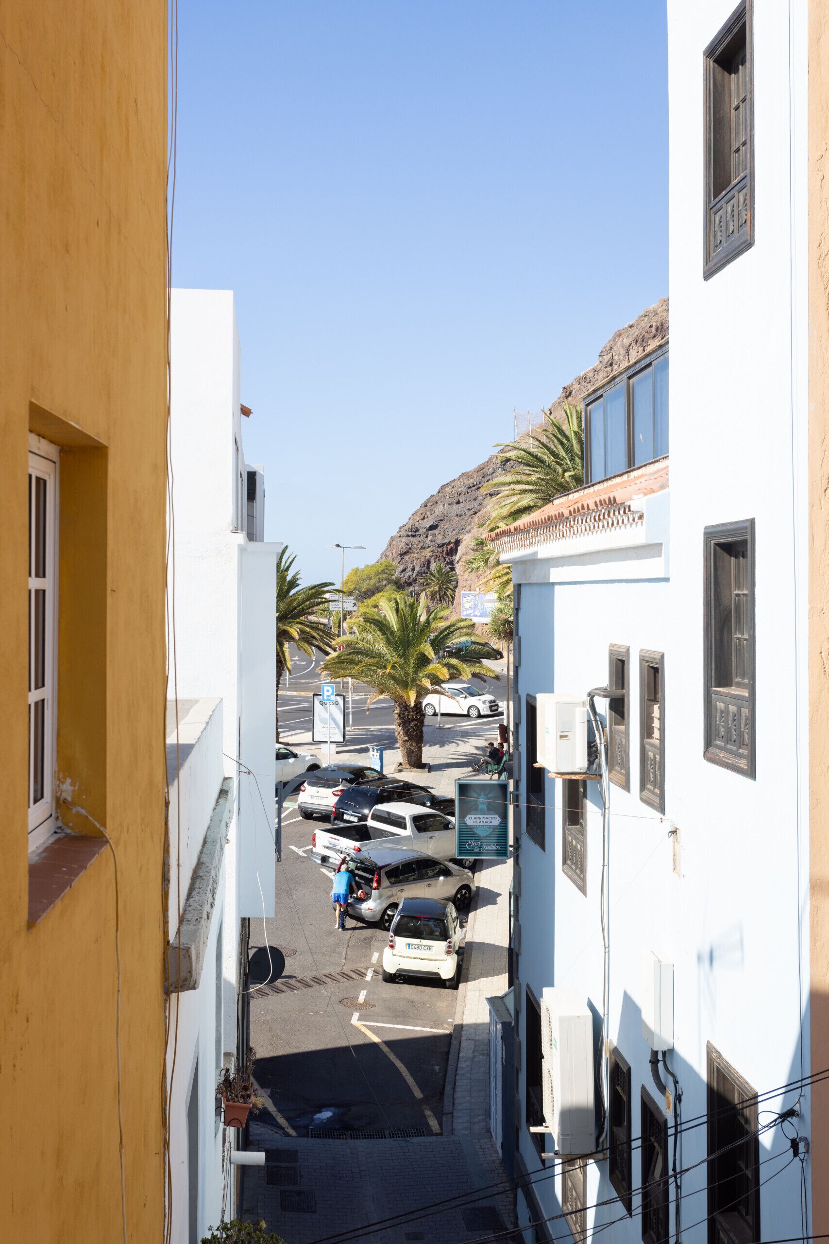 A narrow street with parked cars and buildings on both sides.