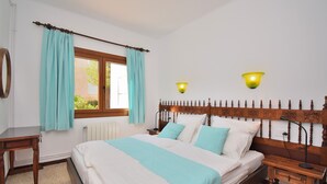Ein Schlafzimmer mit hölzernem Kopfteil, einem Bett mit weißer und hellblauer Bettwäsche, zwei Nachttischen und einem Fenster mit Vorhängen.