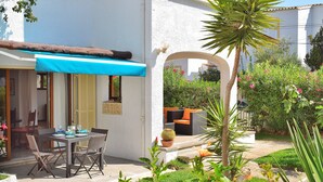 Eine Terrasse im Freien mit Tisch und Stühlen, einem blauen Sonnensegel und einem Kakteus im Topf.