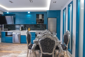 Une cuisine moderne avec des meubles de couleur turquoise, des appareils en acier inoxydable et un coin repas agrémenté de chaises décoratives.
