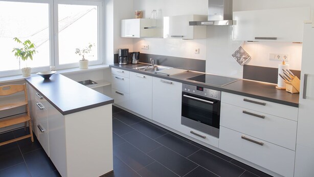 A modern kitchen with white cabinetry, a central island, a built-in oven, and a window providing natural light. - Komfortable, neu Renovierte Few0 im Romantischen Weingut (Leiwen)