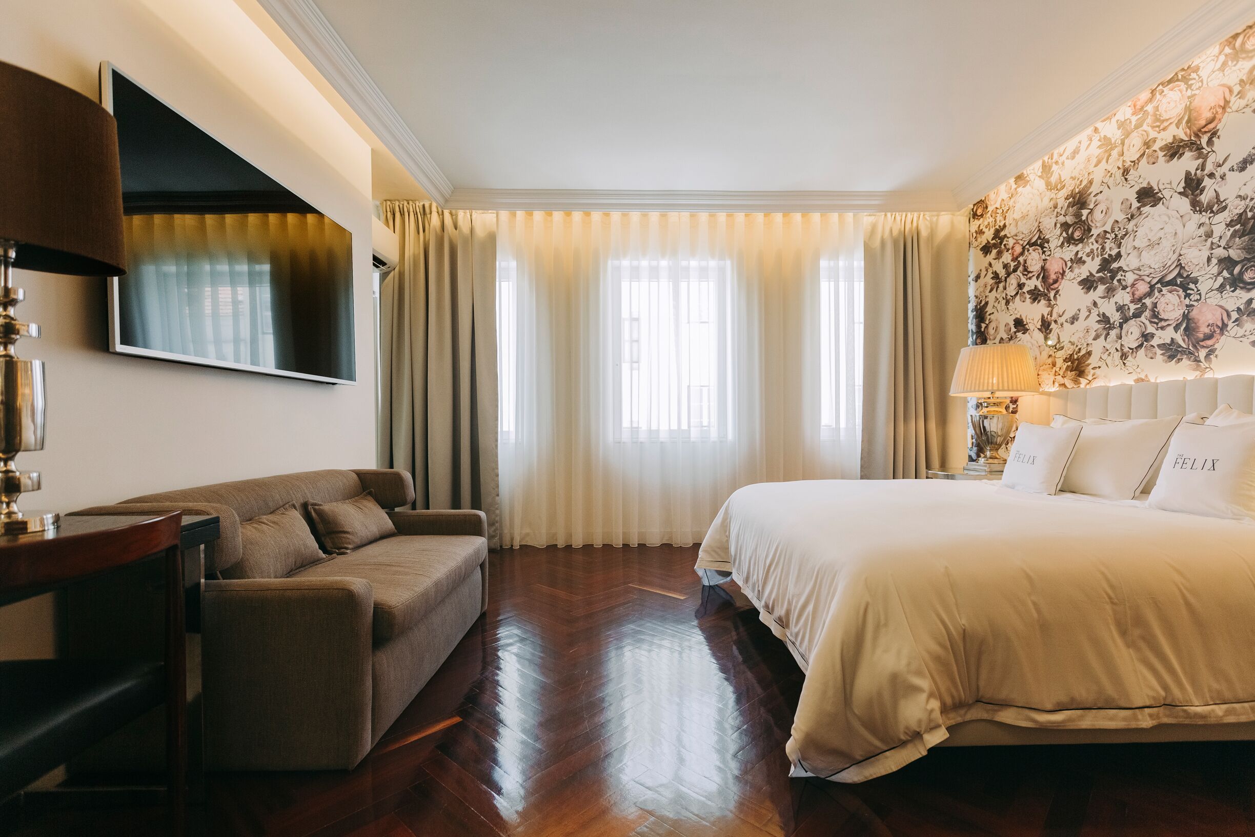 A hotel room with a bed, a sofa, a TV, and a large window with curtains.