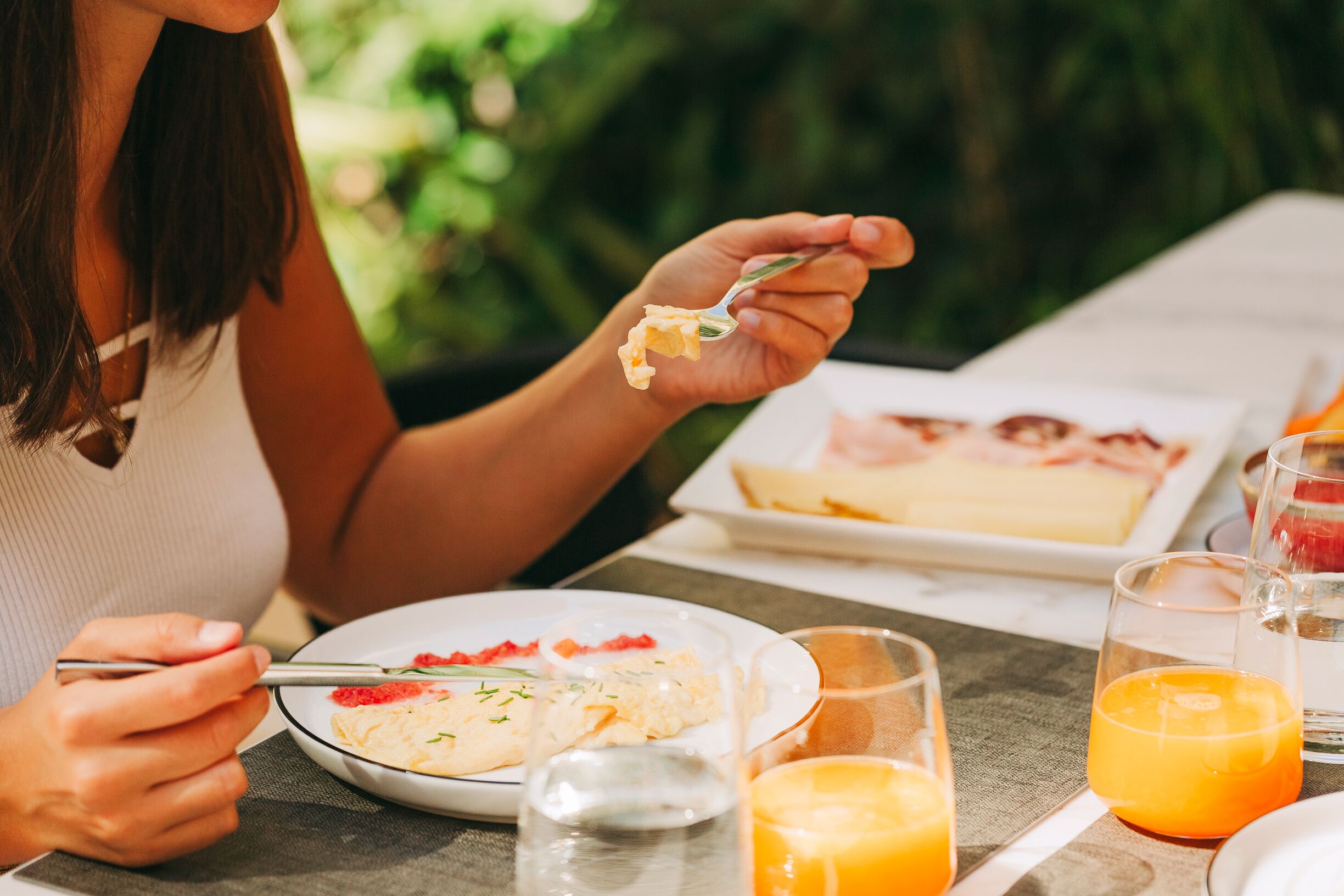 A person eating at an outdoor table with a plate of food, a glass of orange juice, and a glass of water.