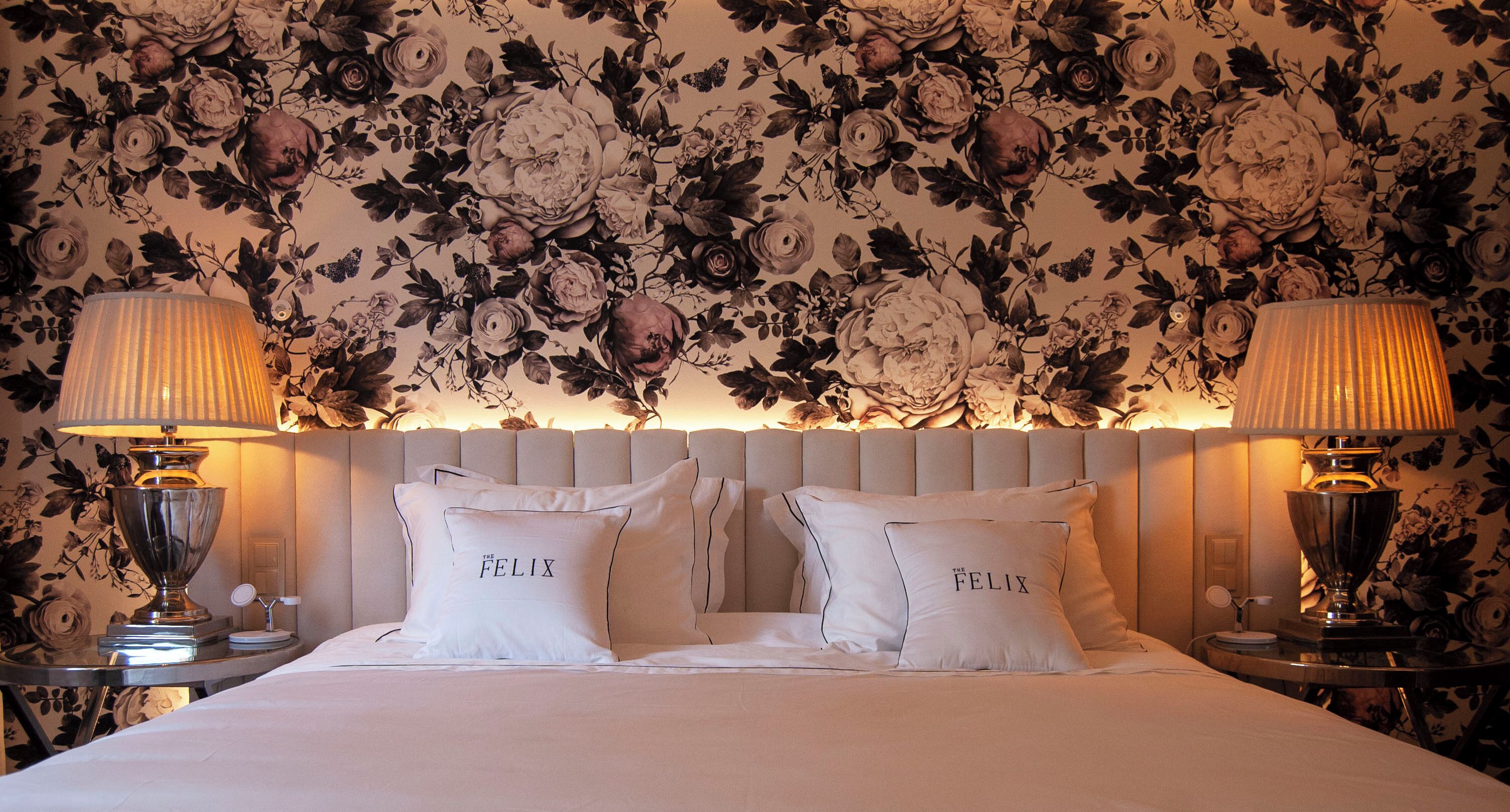 Ett hotellrum med blommig tapet, två sänglampor och kuddar med namnet ”The Felix”.