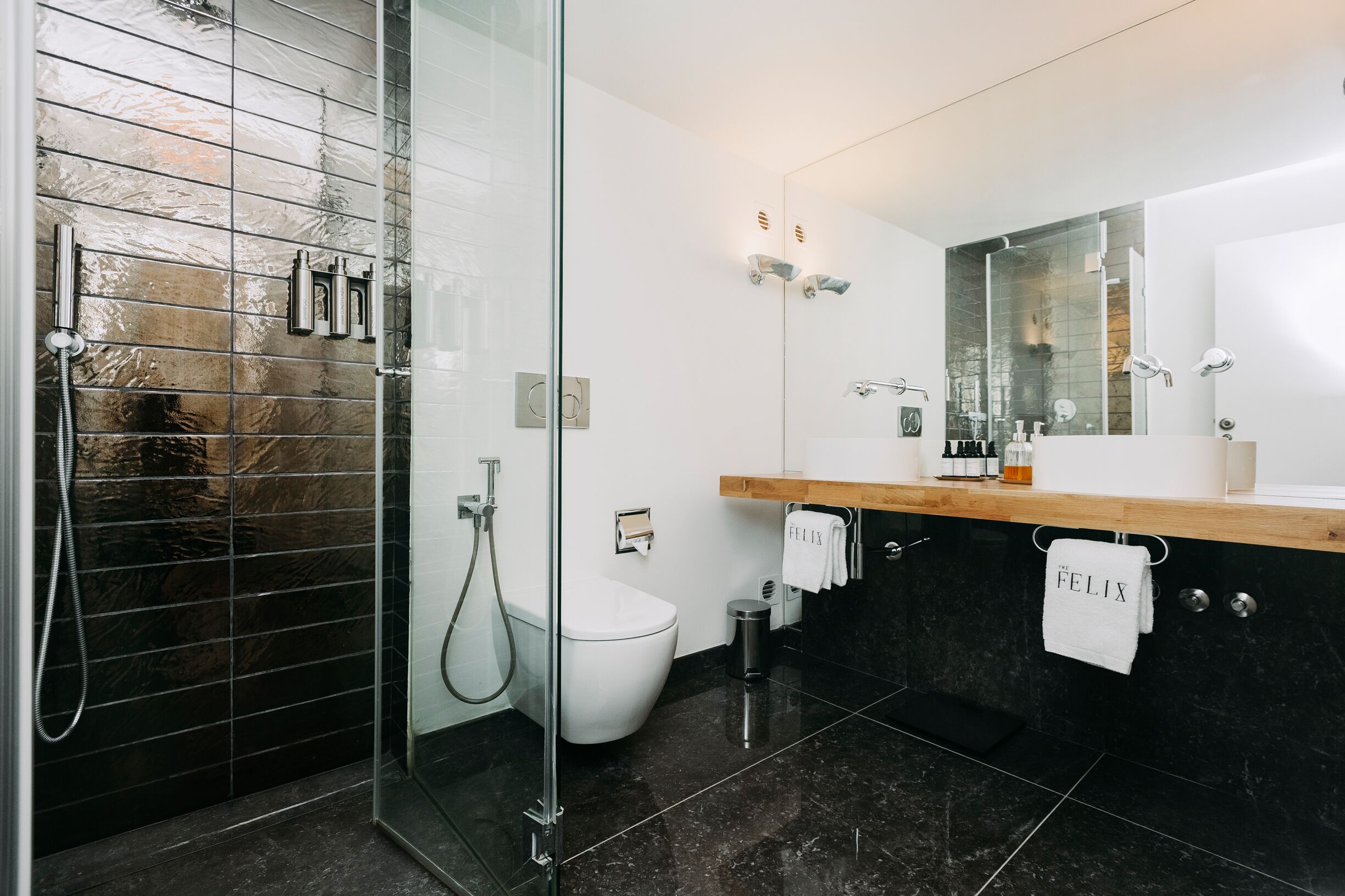 Ein modernes Badezimmer mit einer ein Glasfach raumteilenden Dusche, einer weißen Toilette und einem Waschtisch mit Spiegel.