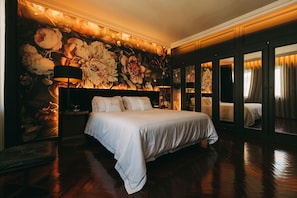 A large bed with white bedding, a nightstand with a lamp, and a floral wallpaper. - The Felix 10 (Lisbon)