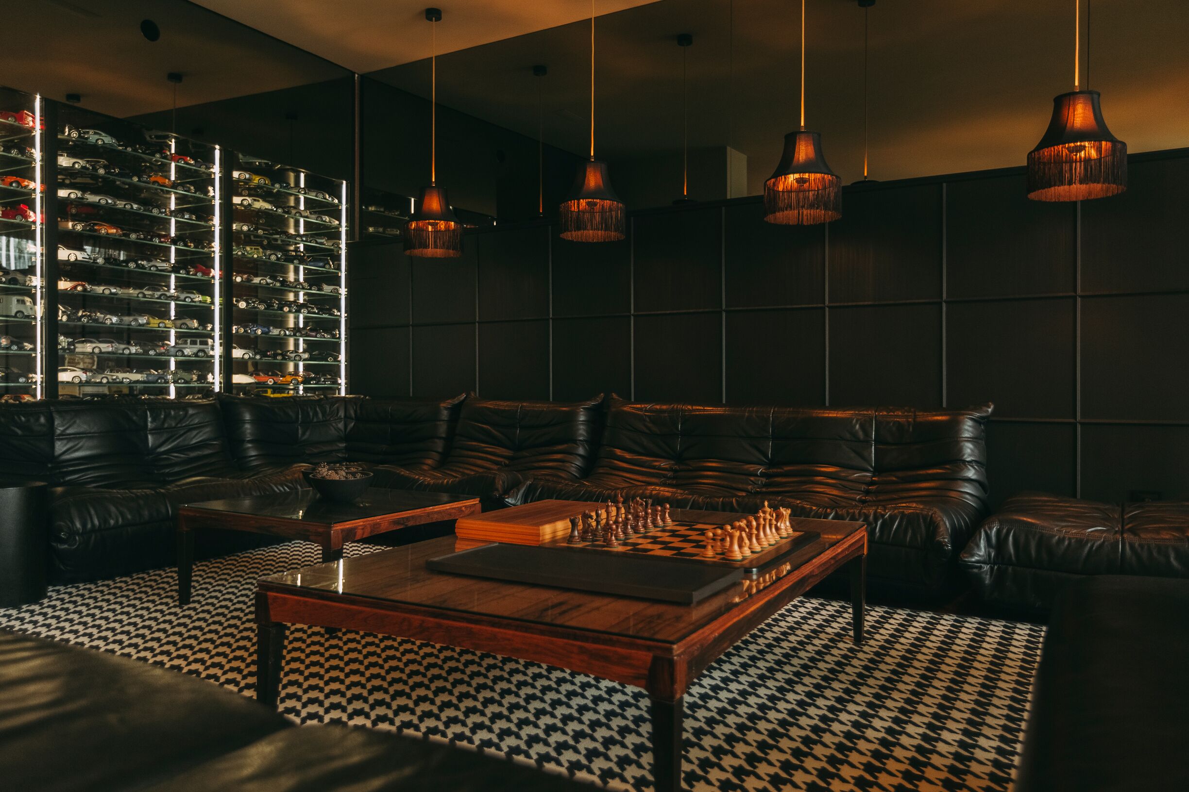 A modern living room with a chessboard, leather sofas, a patterned rug, and a wall of model cars.