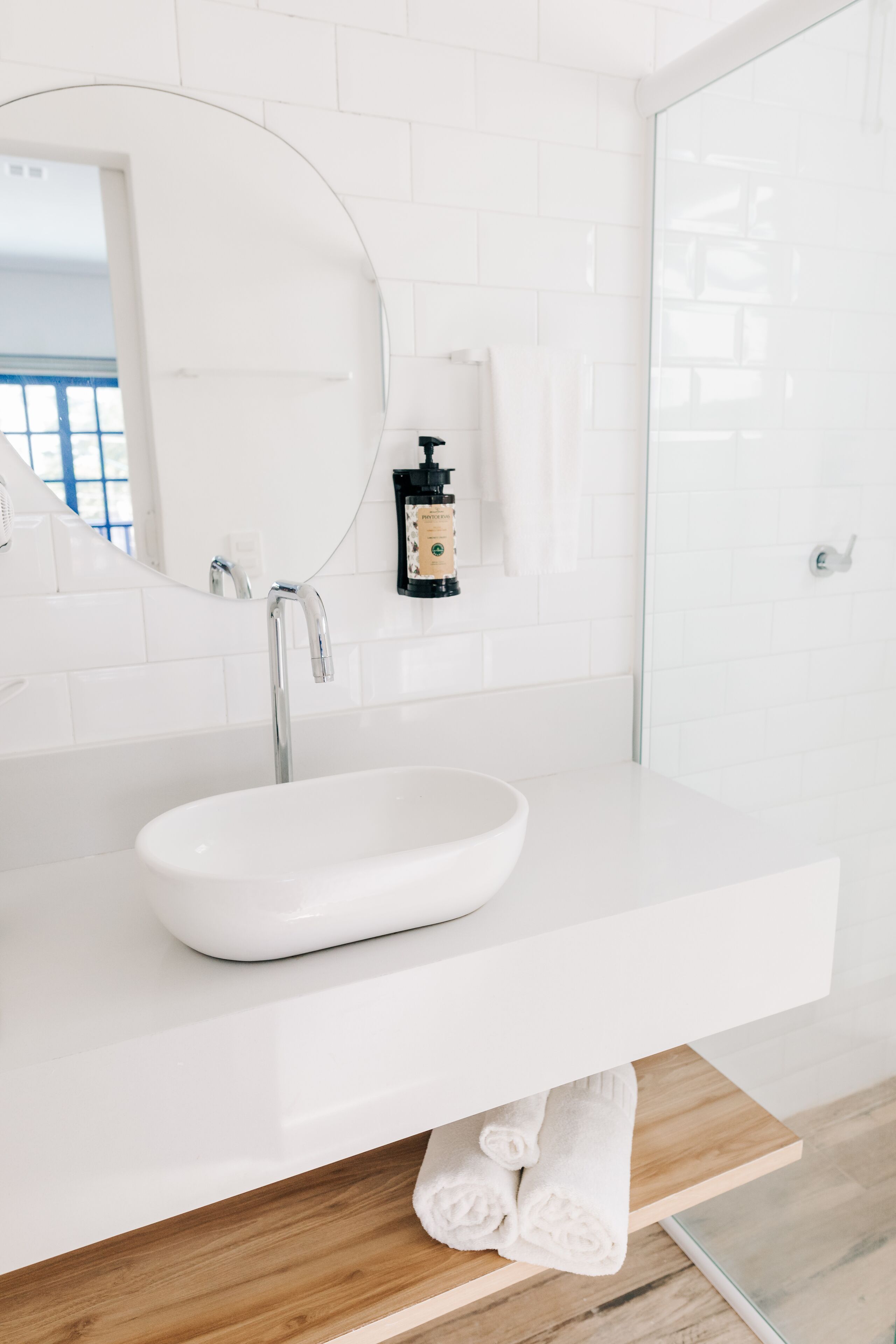 A modern bathroom with a white sink, a round mirror, and a glass shower enclosure.