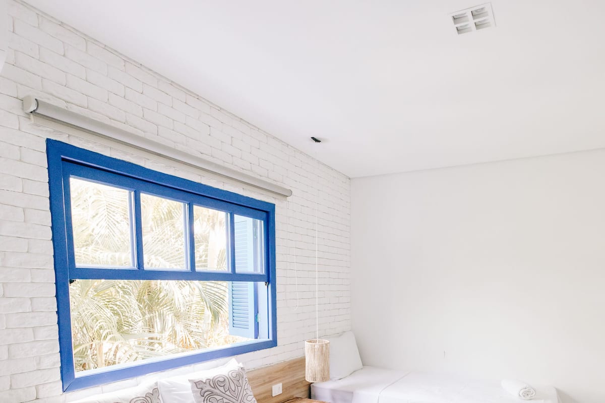 A hotel room with a large bed, a window with blue shutters, white walls, and a white bedspread.