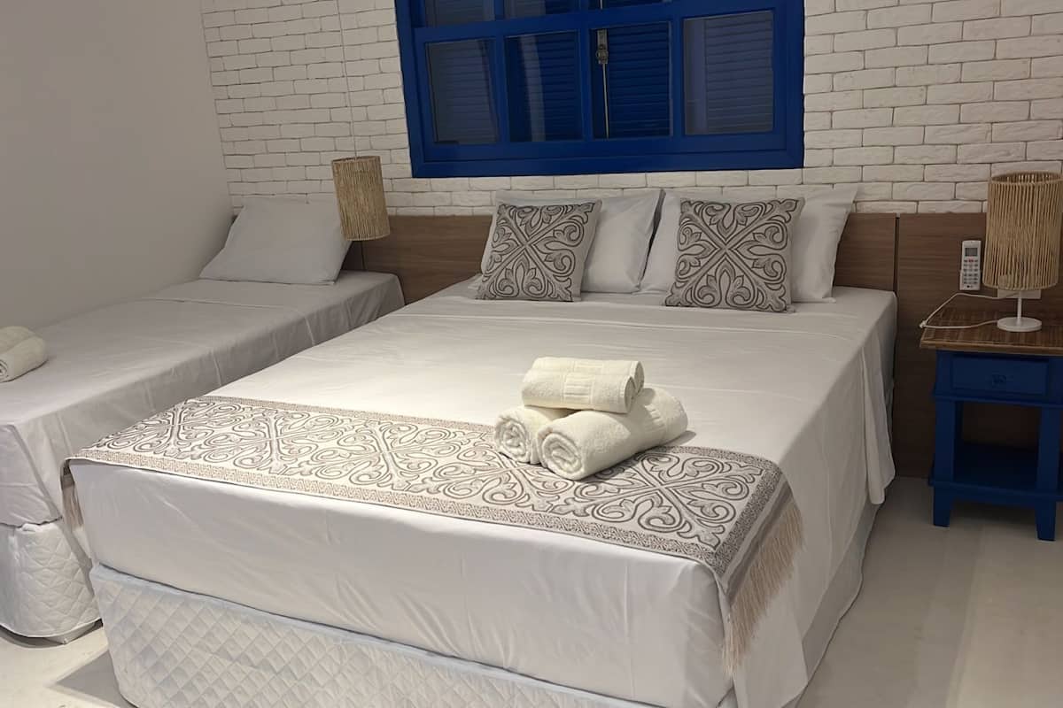 A hotel room with two beds, a blue-framed window, and a bedside table with a lamp.
