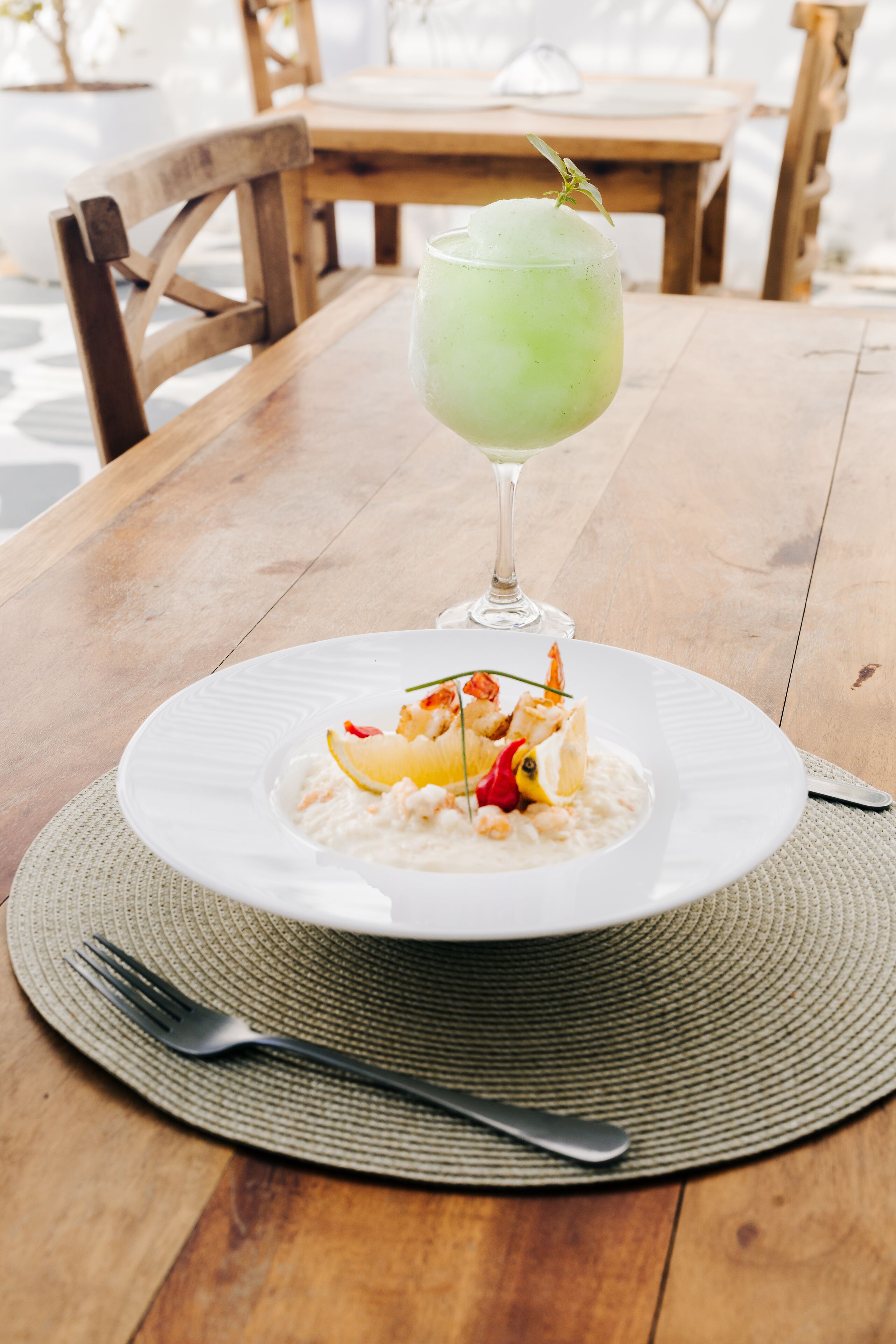 Una mesa de madera con un plato de mariscos blancos, un tenedor y un vaso de bebida verde.