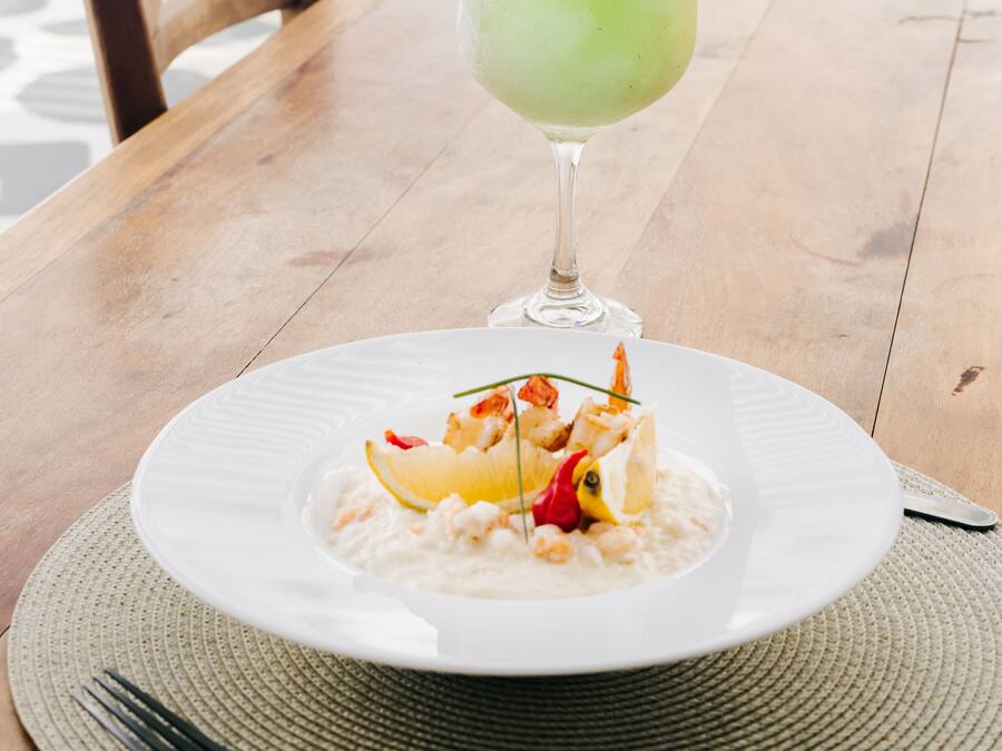 Una mesa de madera con un plato de mariscos blancos, un tenedor y un vaso de bebida verde.