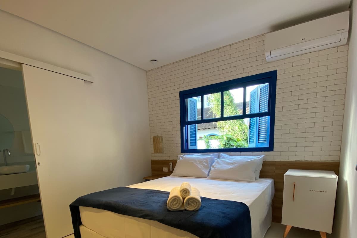 A bedroom with a bed, a window, a nightstand, and a small cabinet.